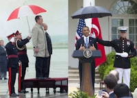 L to R: President George H.W. Bush, under umbrella wearing light coat, reviews honor guard on his arrival to for his summit with Soviet President Gorbachev in Luga, Malta Dec. 1, 1989. With Bush at right is president of Malta, Dr. Vincent Tabona. Others are unidentified. (AP Photo/Doug Mills); Marine holding an umbrella over President Obama at a joint press conference with Turkish Prime Minister Recep Erdogan, May 16, 2013. (Photo: SAUL LOEB/AFP/Getty Images).