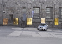 Mikkel Carl, “Brand New Paintings Caught in the Headlights of Parking Cars,” 2013. Mylar emergency blankets (gold), stretchers, cars. Dimensions variable.