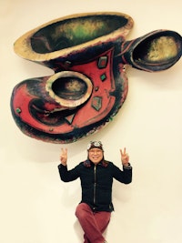 Phong Bui in front of Elizabeth Murray, “Stay Awake” (1989). Oil on canvas laid on wood construction, 70 × 89 × 23 ̋. Courtesy Murray-Holman Family Trust. As exhibited on the Elizabeth Murray Art Wall in its home at Howl! Happening, a new gallery/performance space at 6 East 1st St, just across the street from the Bowery Poetry Club which Elizabeth helped found and which was the site of the original EMAW.