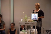 Katrina De Wees holding monitor with video of Jill Sigman in performance of Weed Heart. Photo: Scott Shaw.
