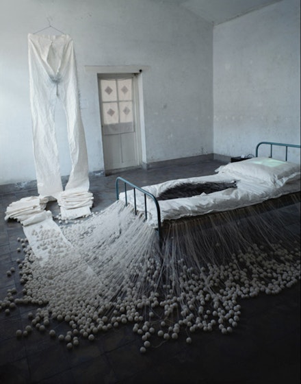 Lin Tianmiao, <em>The Proliferation of Thread Winding</em>, 1995. White cotton thread, rice paper, 20,000 needles (12-15 cm in length), bed, video player, television monitor. Dimensions variable. Open Studio, Baofang Hutong 12#, Beijing, 1995. Collection of the artist. Courtesy Galerie Lelong.