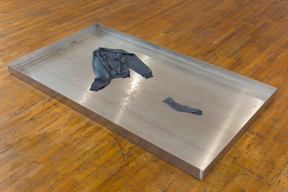 Patrick Staff, <em>Basin</em>, 2018. Aluminum pan, water, glycerine, dog hair, cotton sweater, sock, 4 x 84 x 46.5 inches. Courtesy the artist and Commonwealth and Council. Photo: Ruben Diaz.