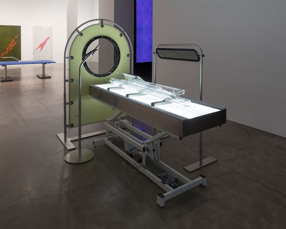 Tauba Auerbach, <em>Non-Invasive Procedure</em>, 2018. Adjustable height medical table, light box, three lenses with stainless steel supports, polarized film, plastic and glass</p>
<p>medical table, lightbox and glass, overall 69 1/2 x 48 x 95 inches. © Tauba Auerbach. Courtesy Paula Cooper Gallery, New York. Photo: Steven Probert.