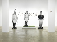 James Luna, <em>Take a Picture with a Real Indian</em>, 1991. Chromogenic silver gelatin, and Polaroid prints, nails, wood, artificial turf, tripod, Polaroid camera, Polaroid film, tape recorder, audio cassette, sound, vinyl text, and chairs, 240 x 76 x 120 inches. Courtesy Garth Greenan Gallery.