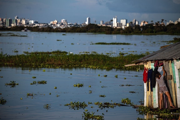 A young woman arranges clothes on the clothesline of her house, a floating one located on the banks of the Rio Negro on the edge of the village of Cacau Pirêra, in Iranduba, Amazonas, Brazil, 2021. Photo: International Monetary Fund/Raphael Alves.
