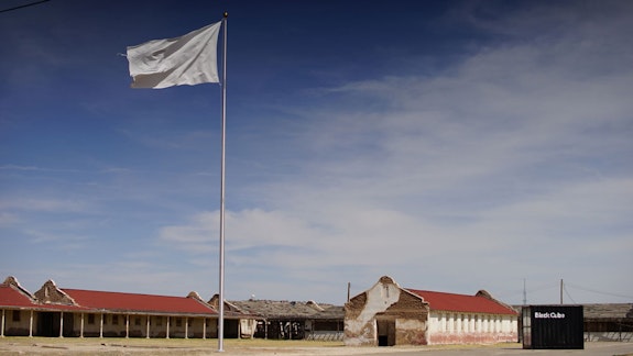 Adriana Corral, <em>Unearthed: Desenterrado</em>, 2018. Site specific, stainless steel flagpole and embroidered golden and bald eagle white cotton flag. Installed, flagpole, 60 feet; flag, 18 x 30 feet. Installation view, Rio Vista Processing Center, Socorro, Texas, 2018. Artwork © Adriana Corral. Courtesy the artist. Image courtesy the artist.