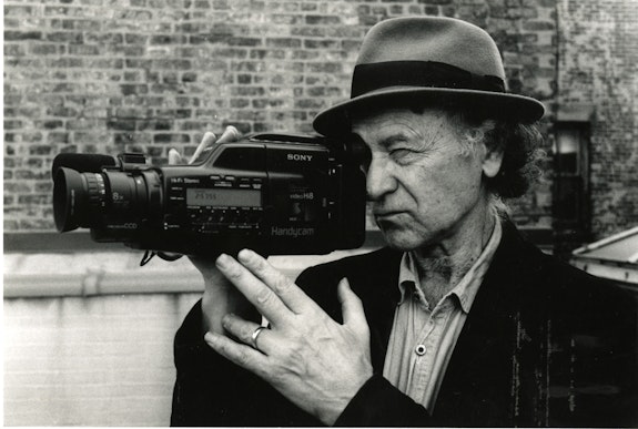 Jonas Mekas with his first Sony video camera in 1987, as seen in <em>Fragments of Paradise</em>, directed by KD Davison. Courtesy the Jonas Mekas estate.
