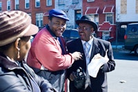 Reverend Robert Jackson, left, jokes with a waiting senior and a Brooklyn College student in front of their building during the Senior Pantry.  Photos by Natalie Keyssar. 